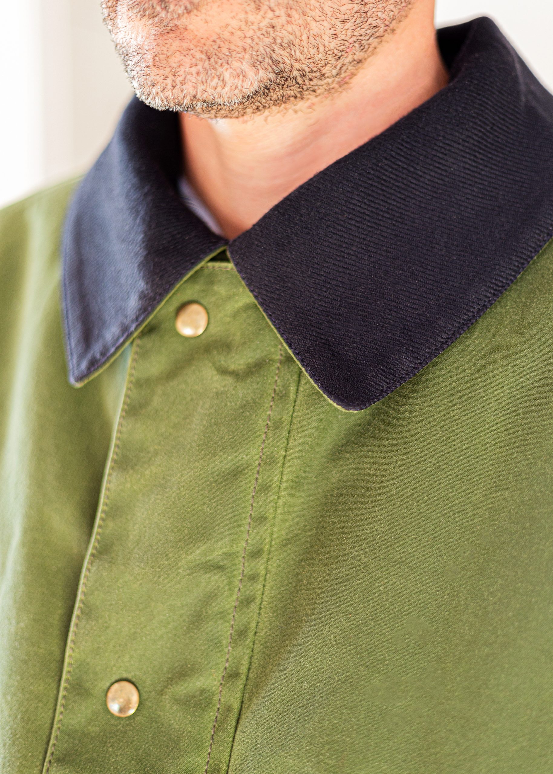 Cuello en sarga de lana marino en contraste con el cuerpo verde del abrigo. Botón automático en oro viejo
