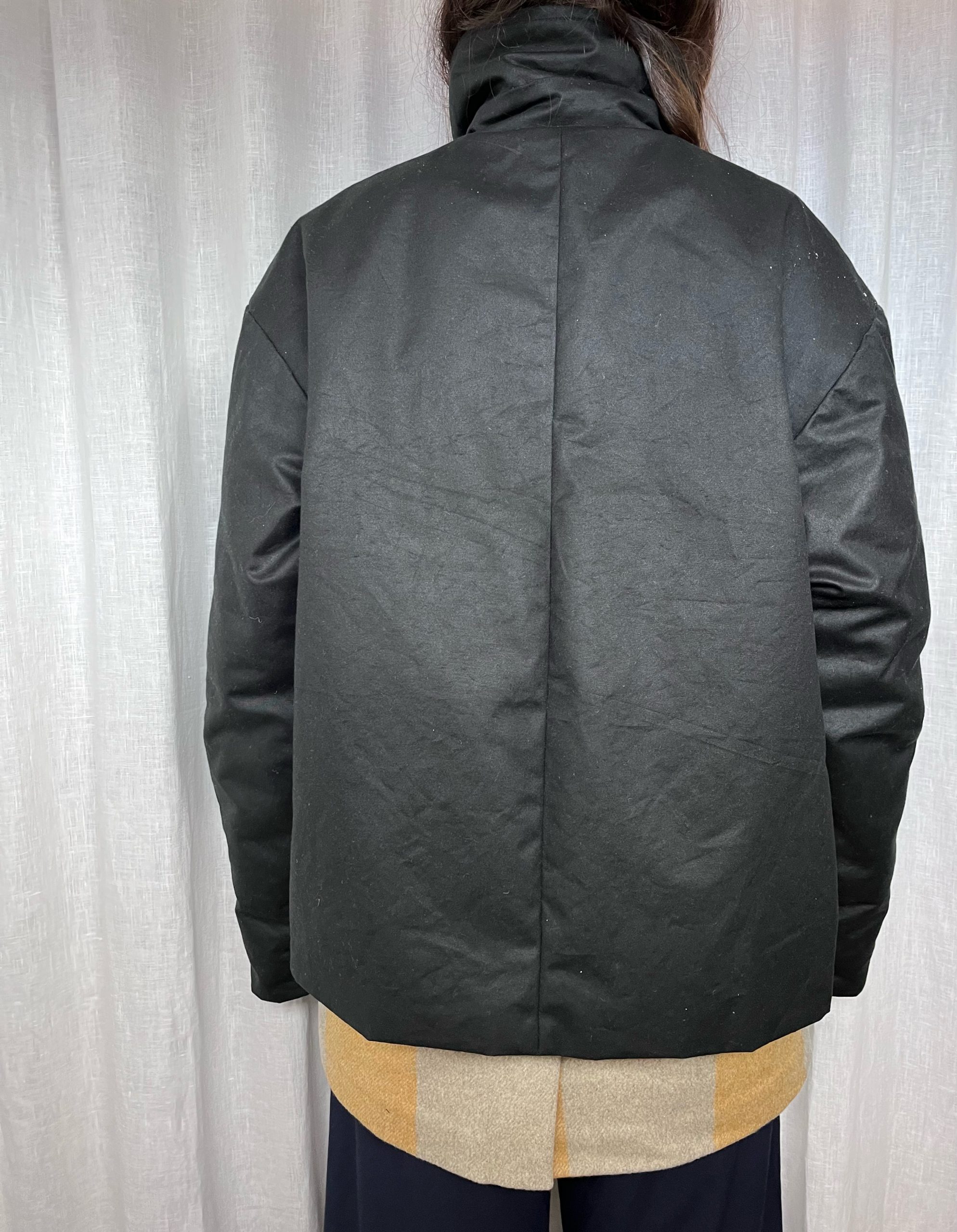 Vista de la espalda. Abrigo Unisex con doble capa. Una impermeable negra y una inferior en lana de cuadros mostaza